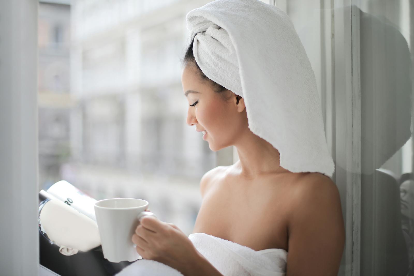 A woman enjoying a quiet moment with coffee and a book in natural light by a window.