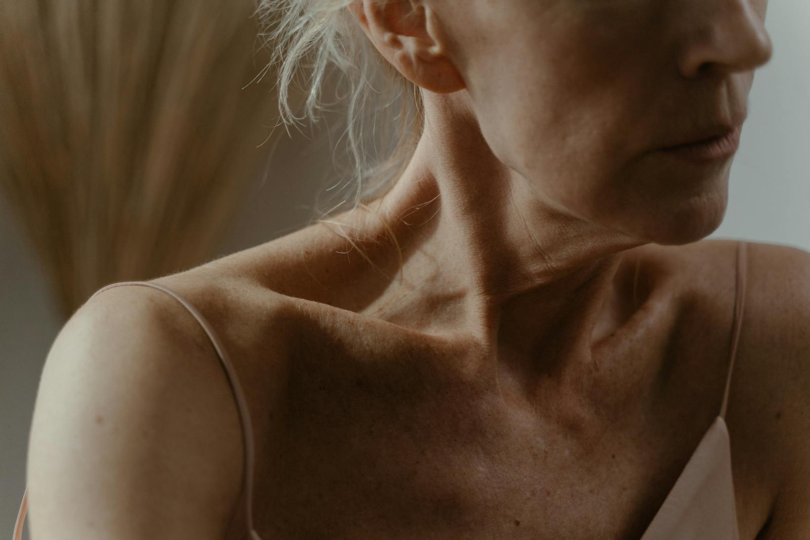 Intimate close-up of an elderly woman's neck and collarbone, highlighting skin texture and veins.